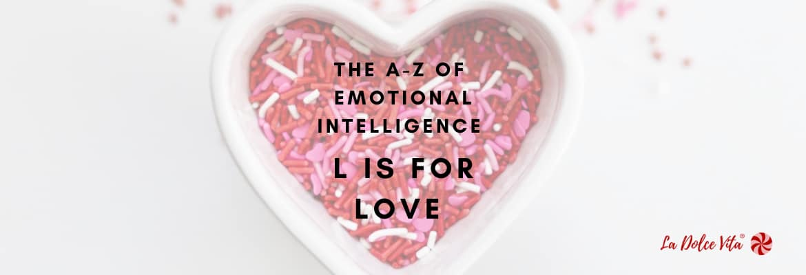 A photo comprising a white background with a heart shaped ramekin of pink and red sprinkles in the middle with black text written over it. The black text reads: The A-Z of Emotional Intelligence, L is for Love